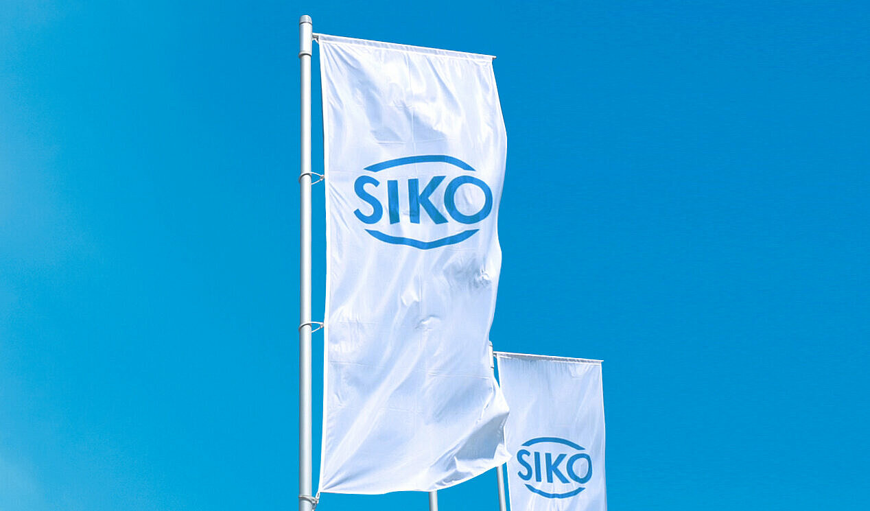 Two white flags with a blue SIKO logo flutter in the wind